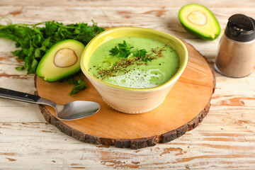 Bowl with green gazpacho and ingredients on light wooden background