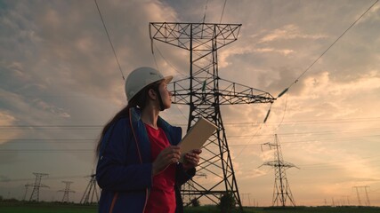 Woman power engineer in a white helmet checks power line using data from electrical sensors on a...