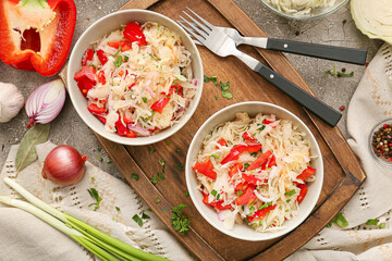 Bowls with tasty sauerkraut and ingredients on grunge background