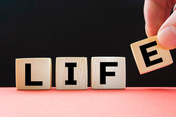 Text LIFE on wooden blocks on a black background. The concept of evolution in time.