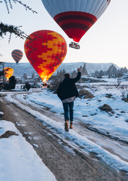 Tourist running toward flying hot air balloons flying up in clou