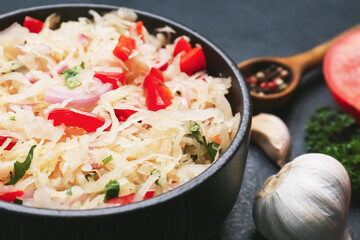 Bowl with tasty sauerkraut and ingredients on dark background, closeup