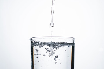 Jet of water or alcohol is pouring into a glass with splashes and bubbles, copy space
