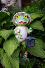 Garden figurine of a frog with lanterns in hand and a small bird. Garden figurine close-up among green leaves