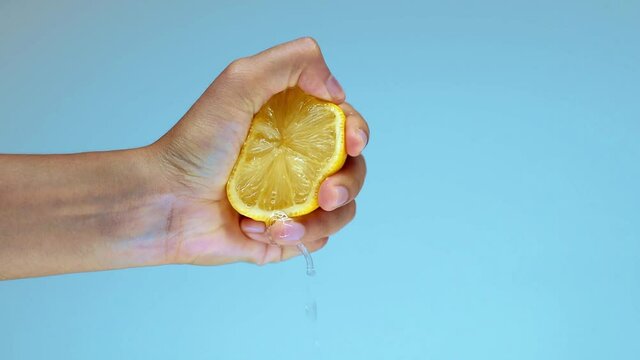 woman squeezing half of lemon isolated on blue background in the studio