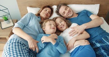 Happy Caucasian family: mom, dad and two children lie in bed in the morning resting and spending time comfortably.