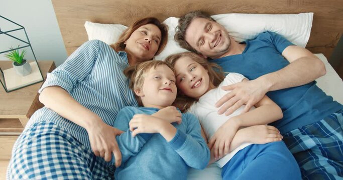 Happy Caucasian family: mom, dad and two children lie in bed in the morning resting and spending time comfortably.