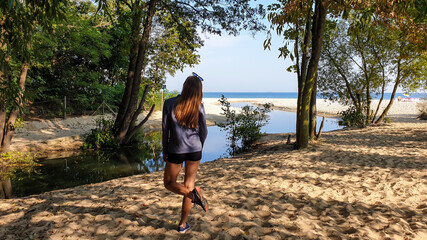 A woman in shorts standing at a confluence of a small river to the Baltic Sea in Poland. There are...