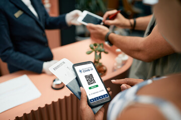 Close-up of woman using digital certificate of coronavirus vaccination during check-in a hotel.