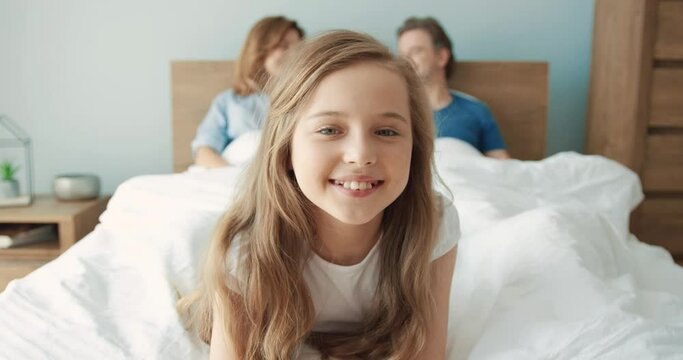 Portrait of cute caucasian preschool girl lying on her parents bed in morning and looking at camera smiling.