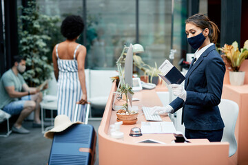 Hotel receptionist using computer while registering guest during coronavirus pandemic.