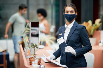 Happy female receptionist with protective face mask working during coronavirus pandemic.