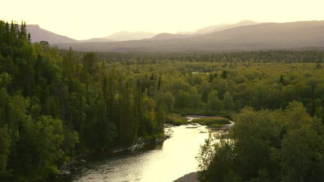 The sun setting over a river in a  green, mountain wilderness.

