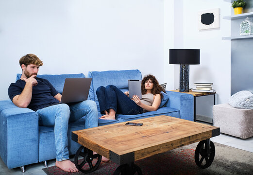 Young couple spending free time with gadgets in modern living room