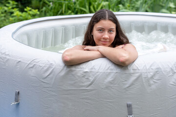 gorgeous teenage girl with long, dark hair relaxes in the garden inflatable pool with jacuzzi