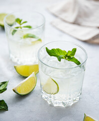 two glasses of lime lemonade mojito with lime slices and mint on white background . Close up