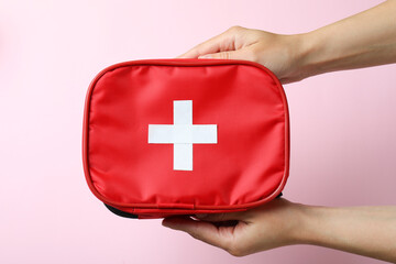 Female hands hold first aid medical kit on pink background