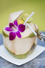 Fresh coconut on a plate with a purple flower and slice of lime and a spoon with a green background