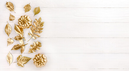 Gold autumn leaves on white wooden background. Autumn concept. Top view of autumn leaves in gold paint on white with copy space for your text