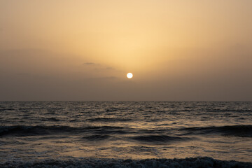 A view of the orange glow in the sky with sun setting in the horizon and waves in the ocean 