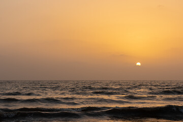 A view of sun setting in the horizon and waves in the ocean