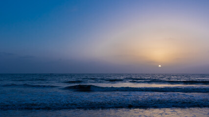 A view of the sky with sun setting in the horizon and waves in the ocean 