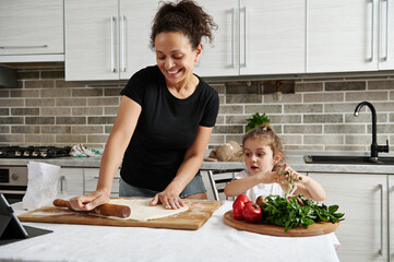 Mom and daughter cook pizza together, roll out the dough with a wooden rolling pin and have fun...