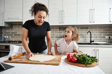 Happy mother and daughter form a round shape of pizza dough, cook together at home. Family spending time concept. Teaching kids how to cook