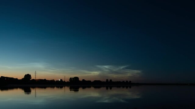 Beautiful time lapse of silvery (noctilucent, polar mesospheric) clouds glowing and shining at summer evening after the sunset over Lake Liepaja (Latvia), calm and tranquil view, wide angle shot