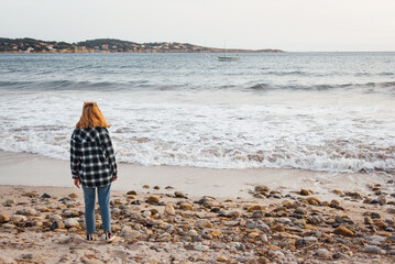 Une jeune femme sur la plage regarde la mer. Une touriste sur la plage hors-saison. Une femme...