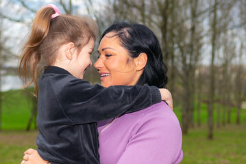 Naklejka premium Beautiful mother and daughter play hugs in a spring park nature in profile looking at each other.
