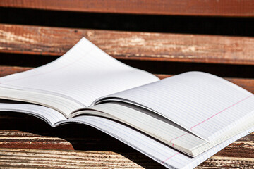Three open notebooks in a ruler on a wooden bench on a sunny day, in bright light, general plan, side shooting