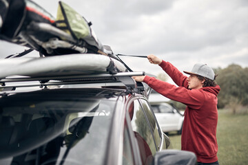 Windsurfer and camper packing and unpacking from a car's roof rack in nature.