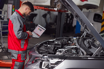 Mechanic using laptop and inspecting car in service