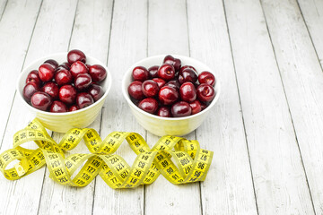 Ripe red cherries in a white dish, centimeter tape on a light wooden background. Concept of healthy food, diet. Top and side view.