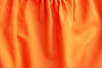 Beautiful orange fabric texture with folds and contrasting shadows . Draped background of bright cotton, texture. Copy space. Close up