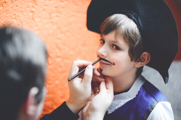 Father making face painting for little kid boy. Child dress up for carnival, halloween or birthday...