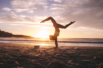 Woman doing yoga pose handstand on beach - Powered by Adobe
