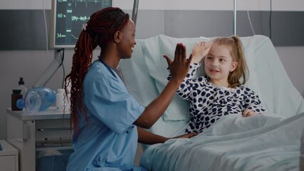 African american pediatrician nurse sitting beside sick child giving high five discussing healthcare treatment during recovery examination in hospital ward. Little kid suffering medicine surgery - Powered by Adobe