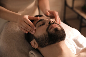 Fototapeta na wymiar Young man receiving facial massage in beauty salon