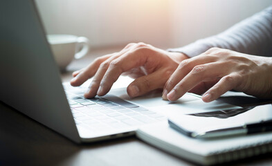 Close-up of man hands using and typing keyboard of laptop computer on office desk. Workspace,...