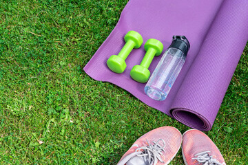 Ladie's dumbbells, fitness mat and sneakers on the green grass background