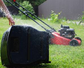 Lawn grass mowing. Washing the lawn mower's grass catcher with water. Splashes of water on a...