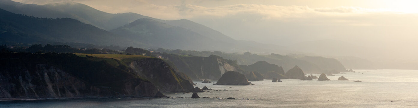 .Panoramic photo view of the steep coast of northern Spain, full of cliffs and rocks that come out of the sea during sunset.
