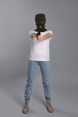 Woman wearing knitted balaclava with gun on grey background