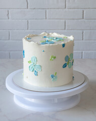 tall white cake on a stand with cream decor blue flowers