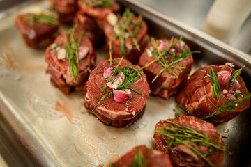 selective view of meat pieces with rosemary and spices on baking sheet