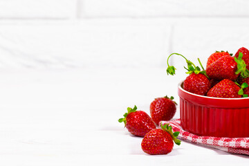 Juicy Fresh Strawberries in a Red Bowl on a white Brick background. Vitamin food. Copy space.