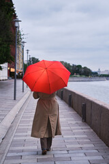 A woman with an umbrella walks along the embankment near the cold river