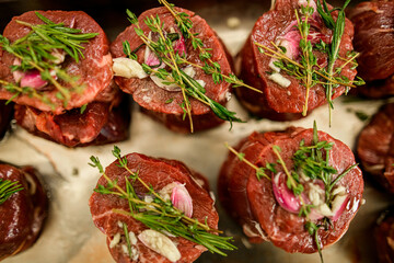close-up of green rosemary sprigs on pieces of raw meat steaks